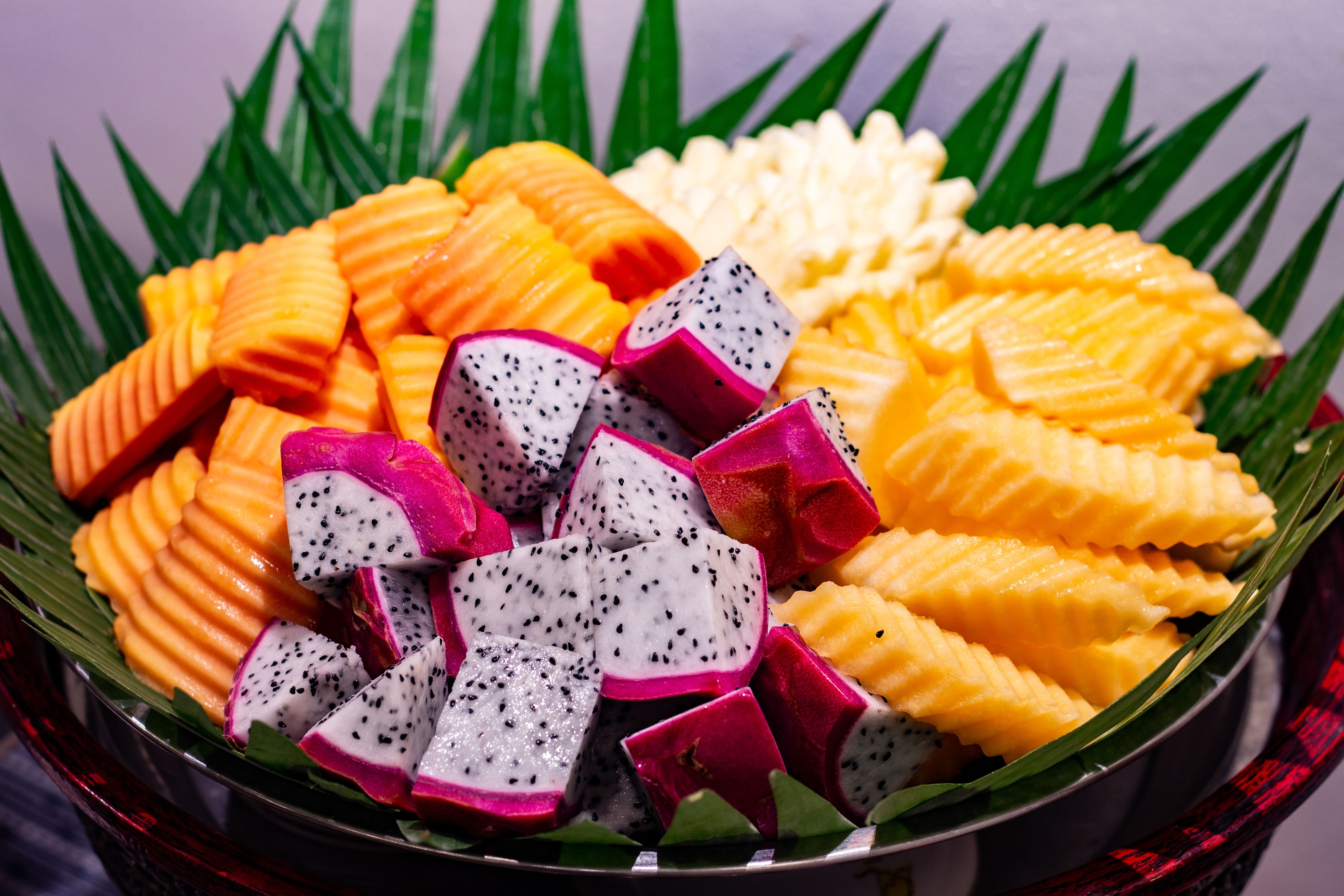 Un bol rempli de tranches de fruit du dragon et de mangue, disposées sur une feuille de bananier.