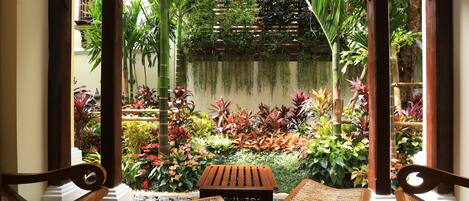 Un conjunto de banco y mesa de madera en un jardín frondoso con diversas plantas y un porche de madera.