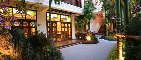 A courtyard with a wooden deck, lush greenery, and a traditional building with a balcony.