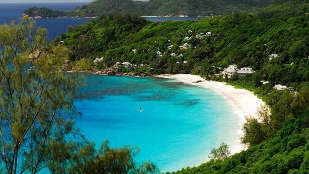 A coastal area with a sandy beach, clear turquoise waters, and lush green hills. - Hotel Bel Air (Mahé Island)