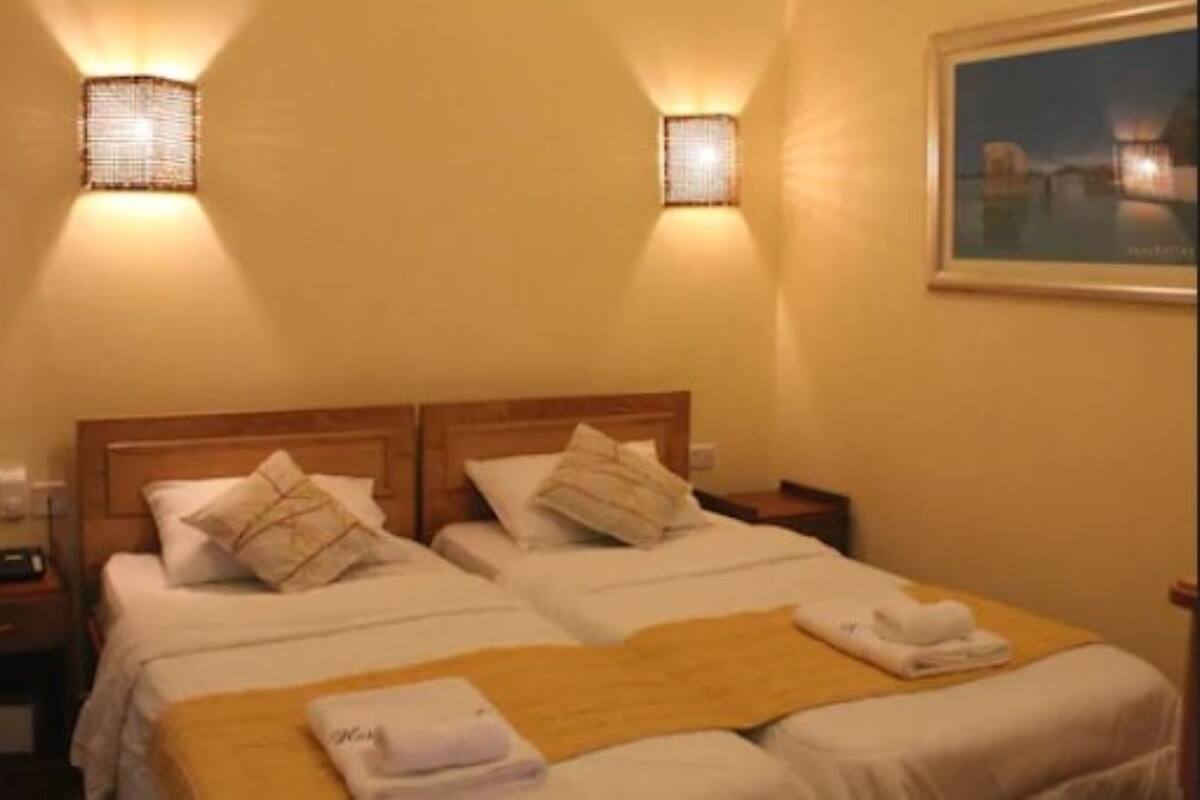 A hotel room with two beds, a wooden headboard, bedside tables, and wall-mounted lamps.