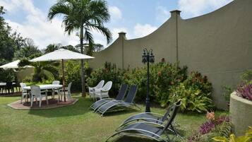 A patio area with a table and chairs, a lounge chair, and a palm tree.