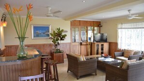 A spacious living area with wicker furniture, a wooden bar, and a large window with curtains. - Hotel Bel Air (Mahé Island)