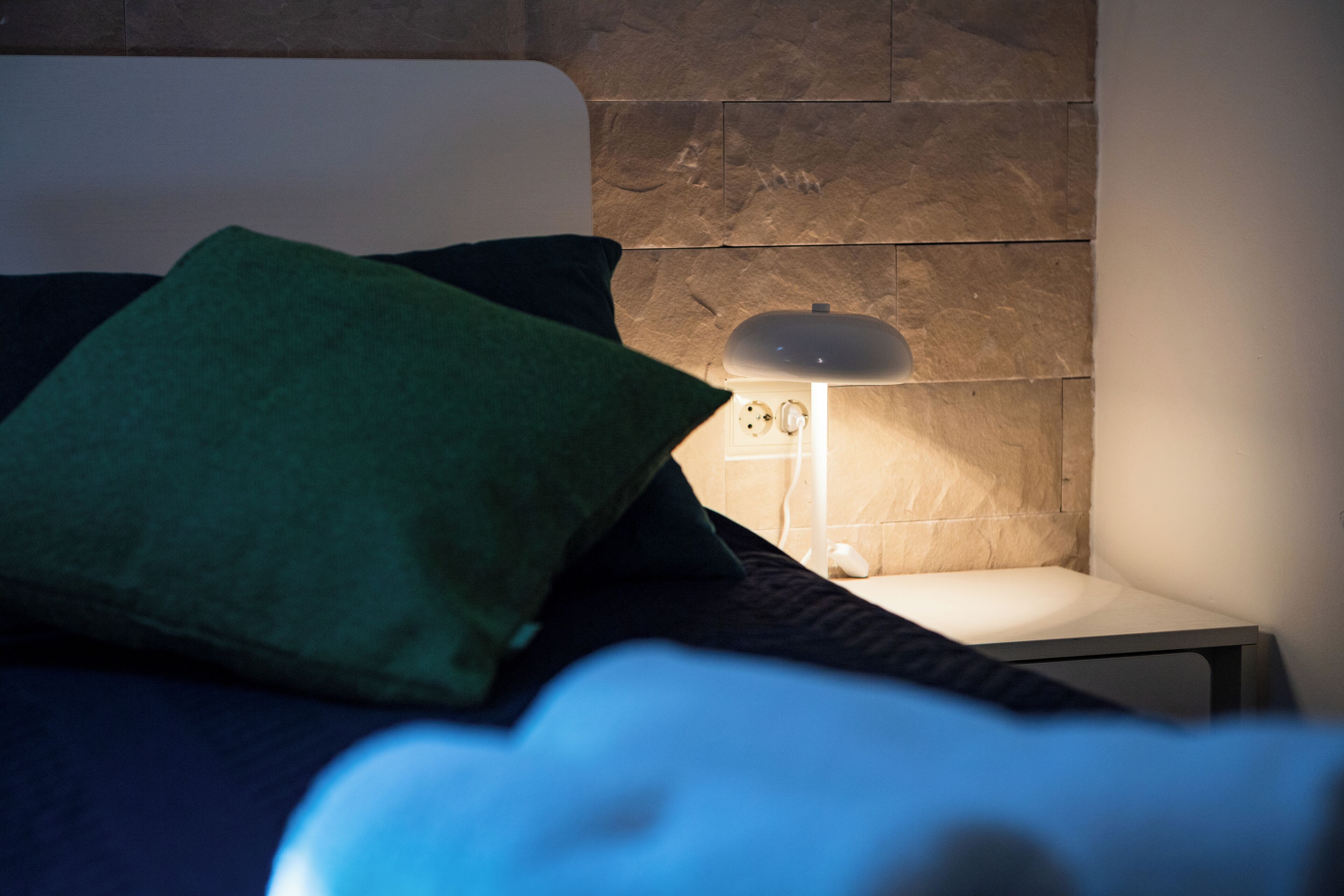 Un lit avec un oreiller vert, une tête de lit blanche et une table de chevet avec une lampe.