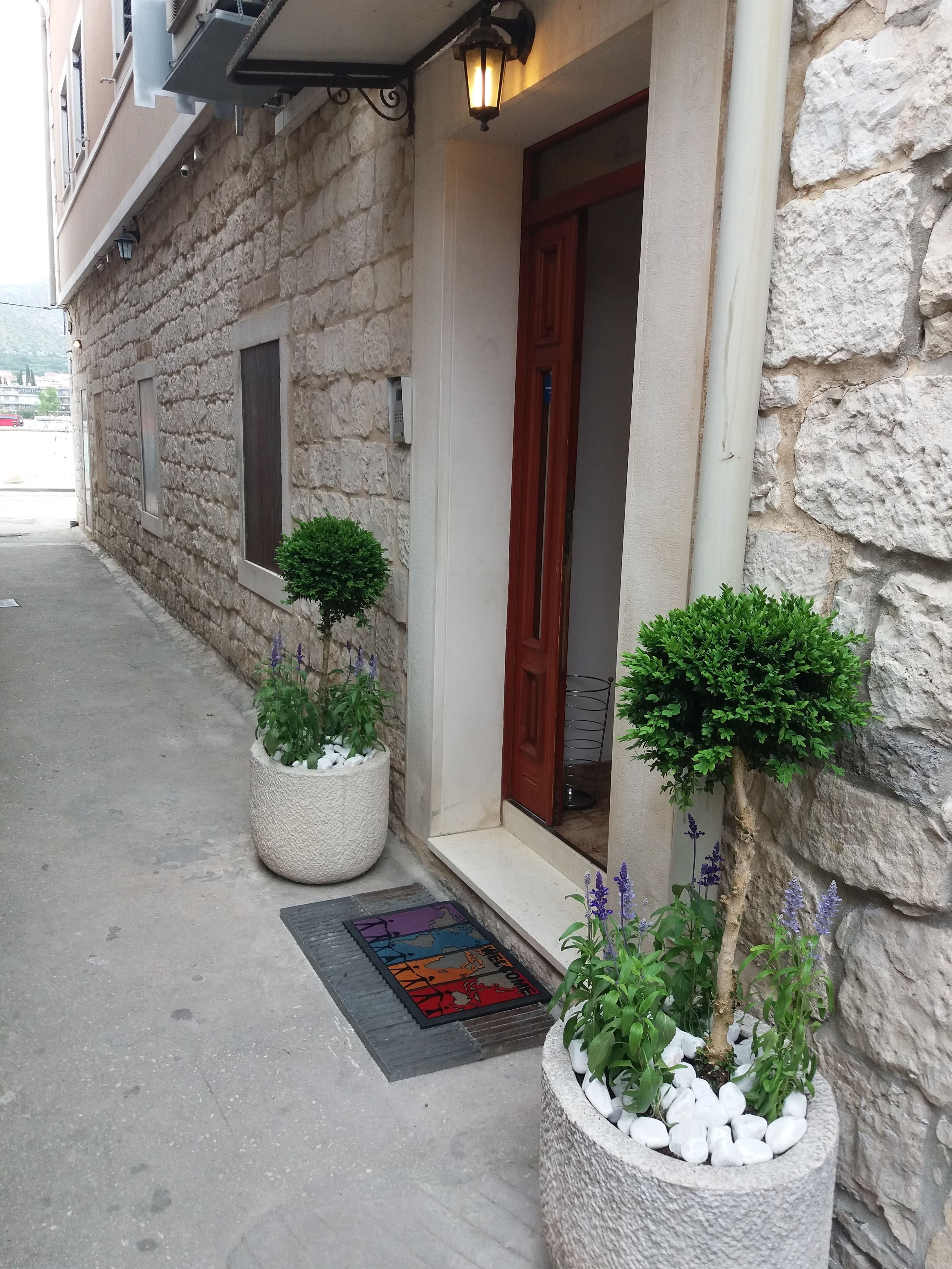A stone building with a wooden door, potted plants, and a colorful doormat.