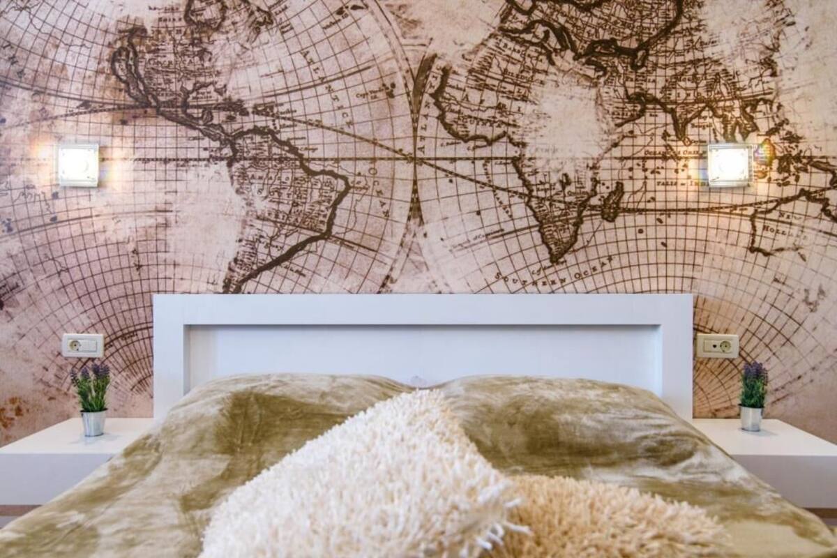 A bedroom with a world map wall, a white headboard, and two bedside lamps.