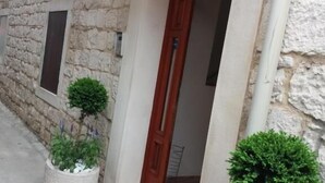 A stone building with a wooden door, a small potted plant, and a colorful mat at the entrance.