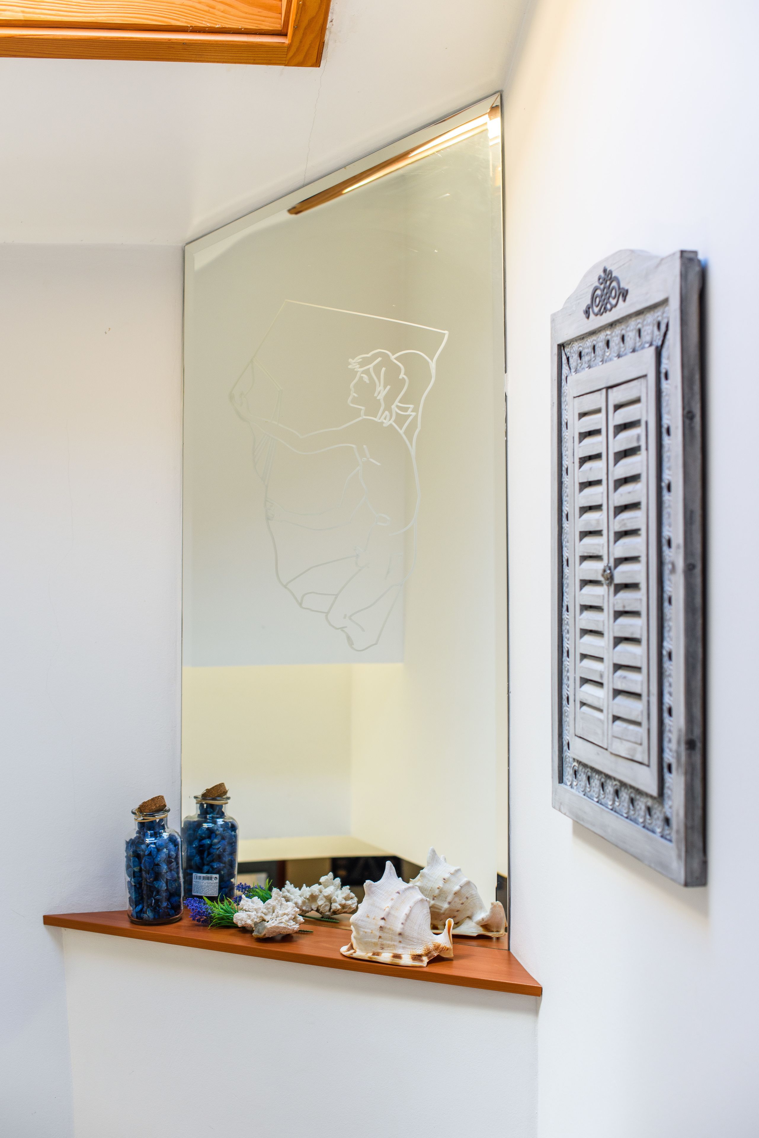 A bathroom with a large mirror, a shelf with decorative items, and a wall-mounted vent.