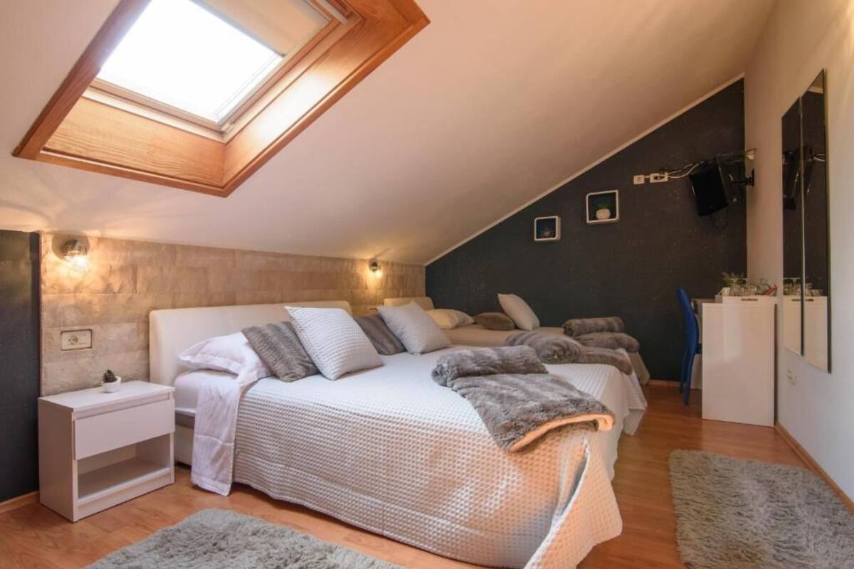 A bedroom with a skylight, a bed with multiple pillows, a nightstand, a desk, and a mirror.