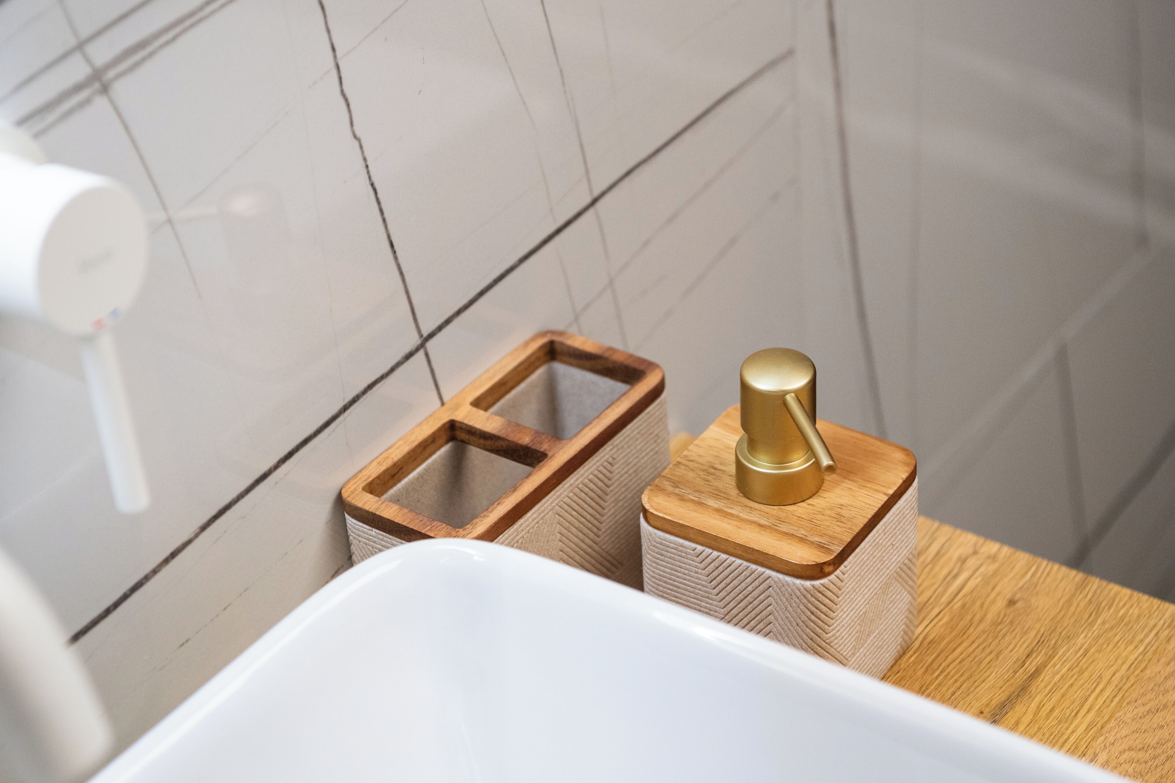 A bathroom with a white sink, wooden and woven storage containers, and a gold-colored soap dispenser.