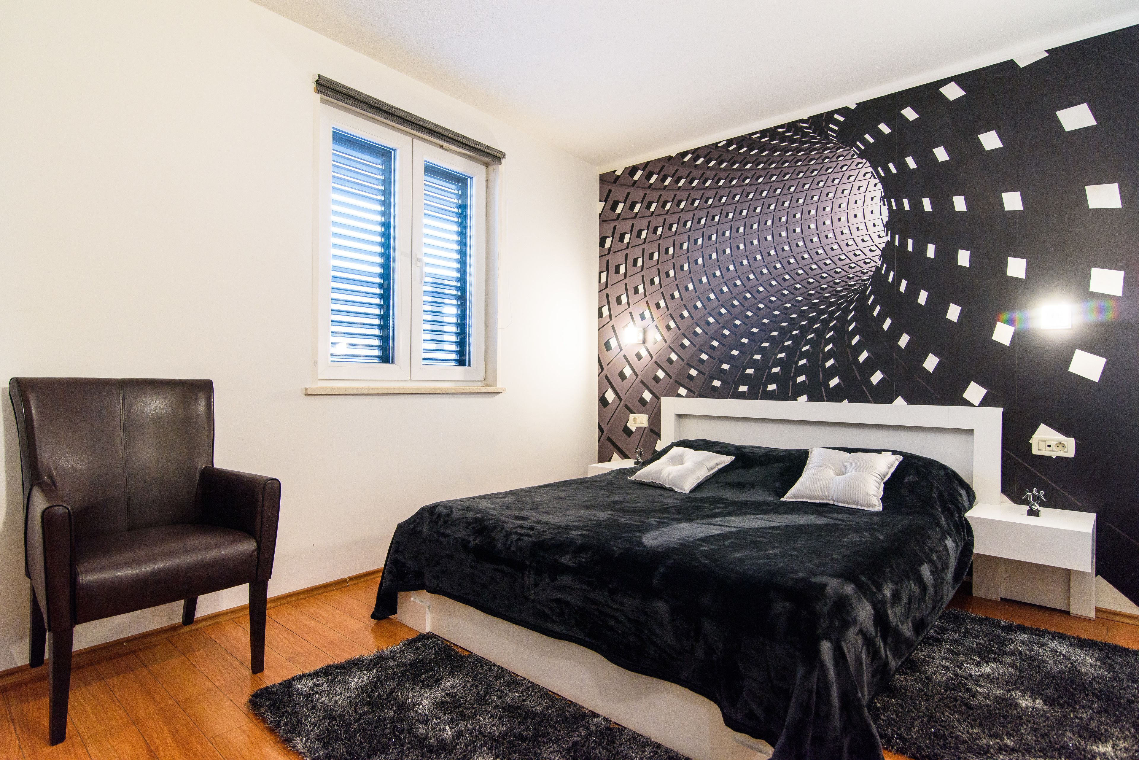 Een slaapkamer met een bed, een stoel, een raam en een muur met een geometrisch patroon.