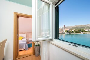 A room with a bed, a window with a view of a body of water and a distant building, and a potted plant. - Villa Jidro (Trogir)