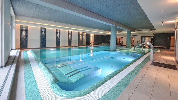 Una piscina interior con agua cristalina, bordes de azulejos y diseño moderno.