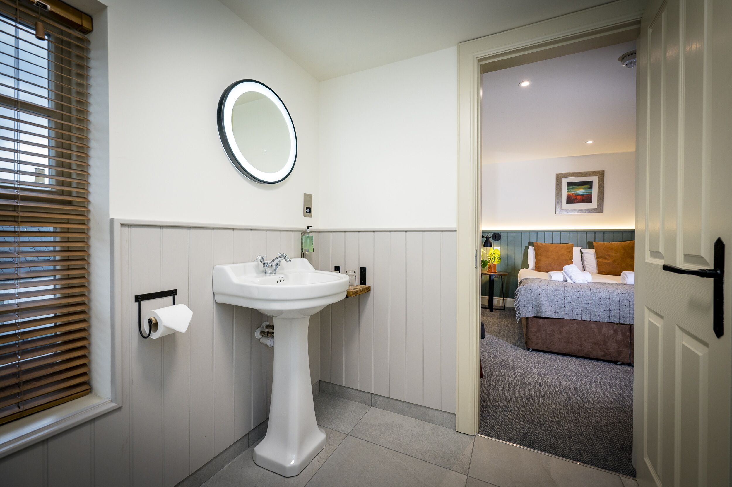 A bathroom with a pedestal sink, toilet paper holder, and a mirror.