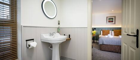 A bathroom with a pedestal sink, toilet paper holder, and a mirror.