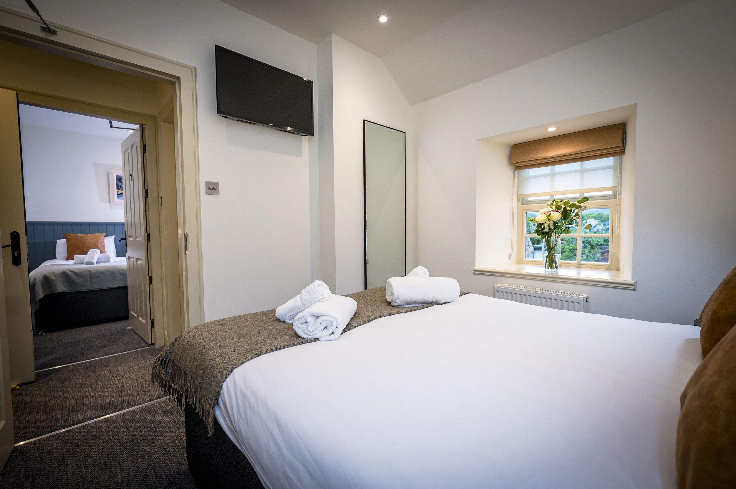 A hotel room with a large bed, a smaller bed, a TV, a window with a view, and a door leading to another room.