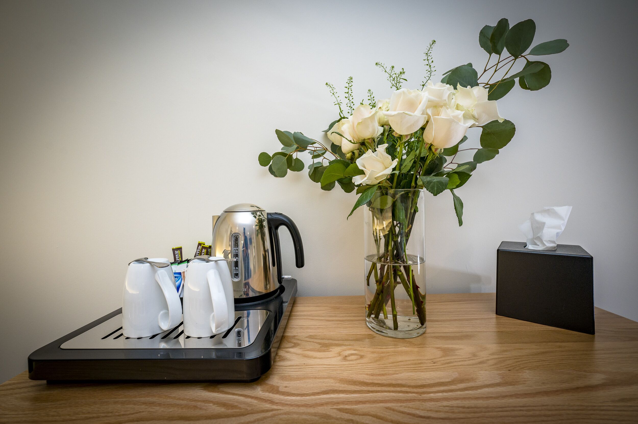 A coffee maker, a vase with white flowers, and a tissue box on a wooden table.