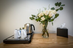 Una cafetera, un florero con flores blancas y una caja de pañuelos sobre una mesa de madera.