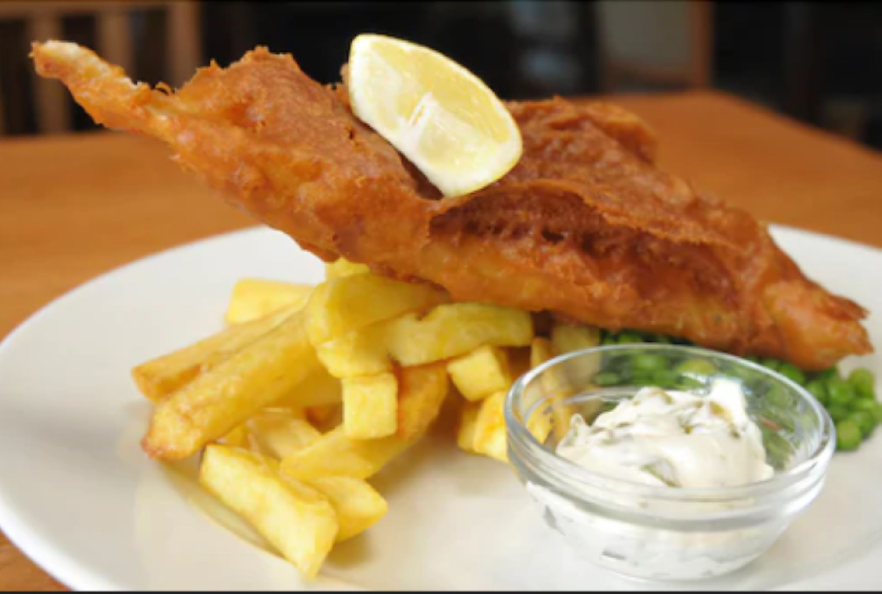 Une assiette avec du poisson-frites, un quartier de citron et un petit bol de sauce.