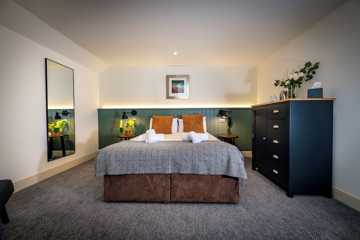 A neatly arranged bedroom with a large bed, bedside tables, a dresser, a mirror, and a framed picture on the wall.