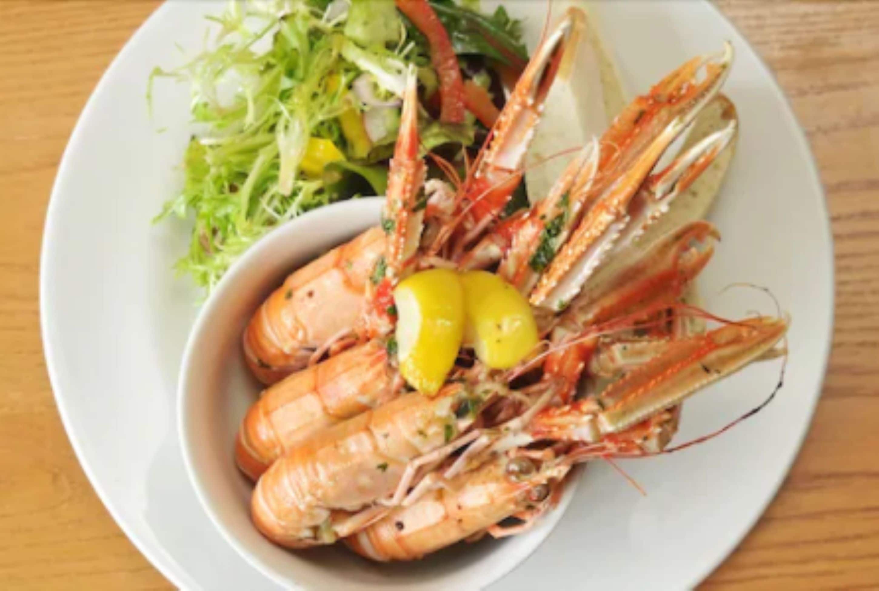 A plate of cooked prawns with lemon wedges and a side salad.