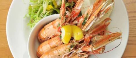 Une assiette de crevettes cuites, accompagnée de quartiers de citron et d’une salade.