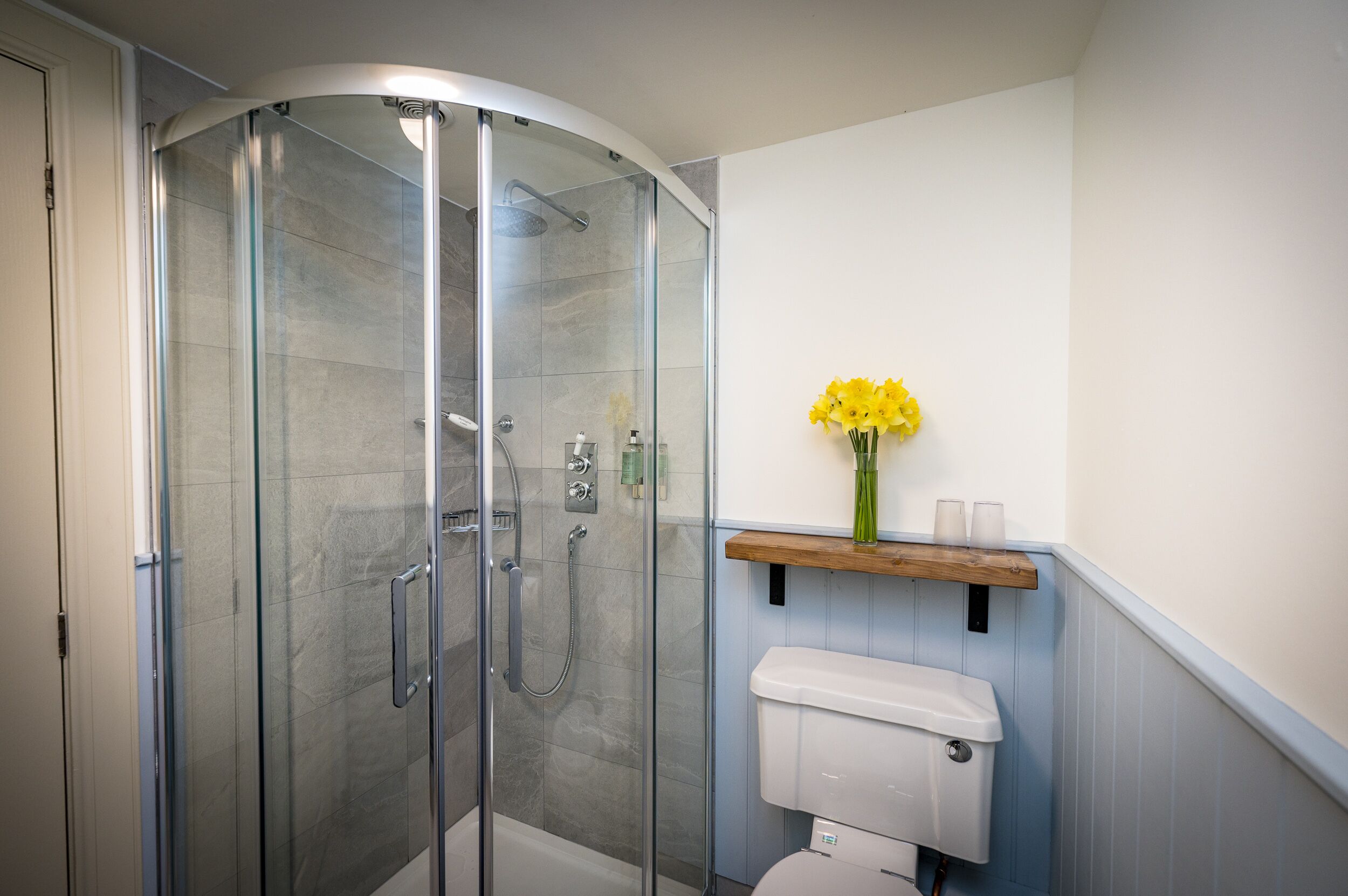 Ein modernes Badezimmer mit einer Duschkabine, einer Toilette und einem Regal mit einer Vase voller gelber Blumen.