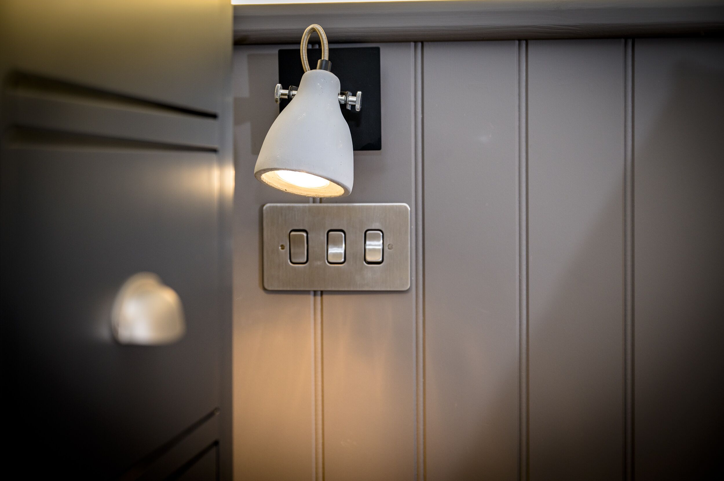 A wall-mounted light fixture with a white shade and three switches.