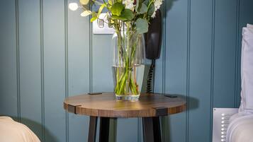 Una habitación con una mesa de madera que sostiene un florero con flores, una lámpara y un teléfono.