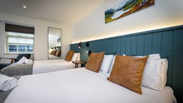 Habitación de hotel con dos camas, una mesita redonda pequeña, una silla, un espejo grande y un cuadro en la pared.