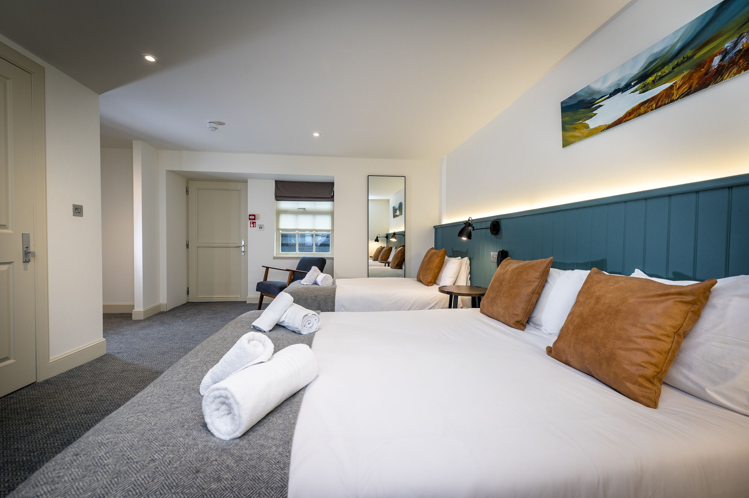 Habitación de hotel con dos camas, un espejo grande, un cuadro en la pared y vista al pasillo.