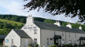 Un edificio blanco con un letrero que dice "Loch Ness Inn" y un camino pavimentado al frente.