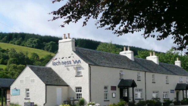 A white building with a sign reading "Loch Ness Inn" and a paved road in front.