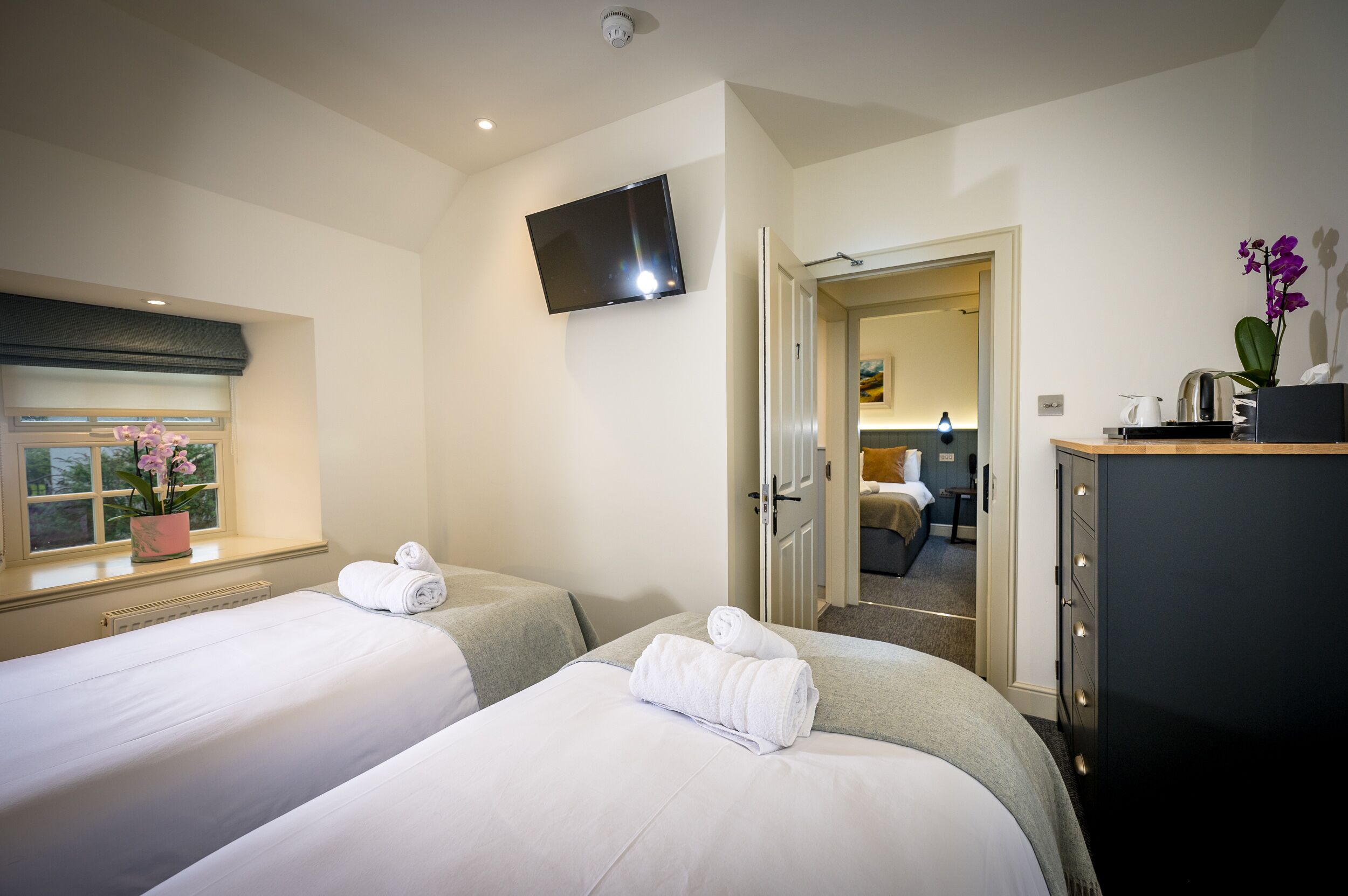 Ein Hotelzimmer mit zwei Betten, einem Fernseher, einem Fenster mit Blick und einer Tür zu einem weiteren Zimmer.