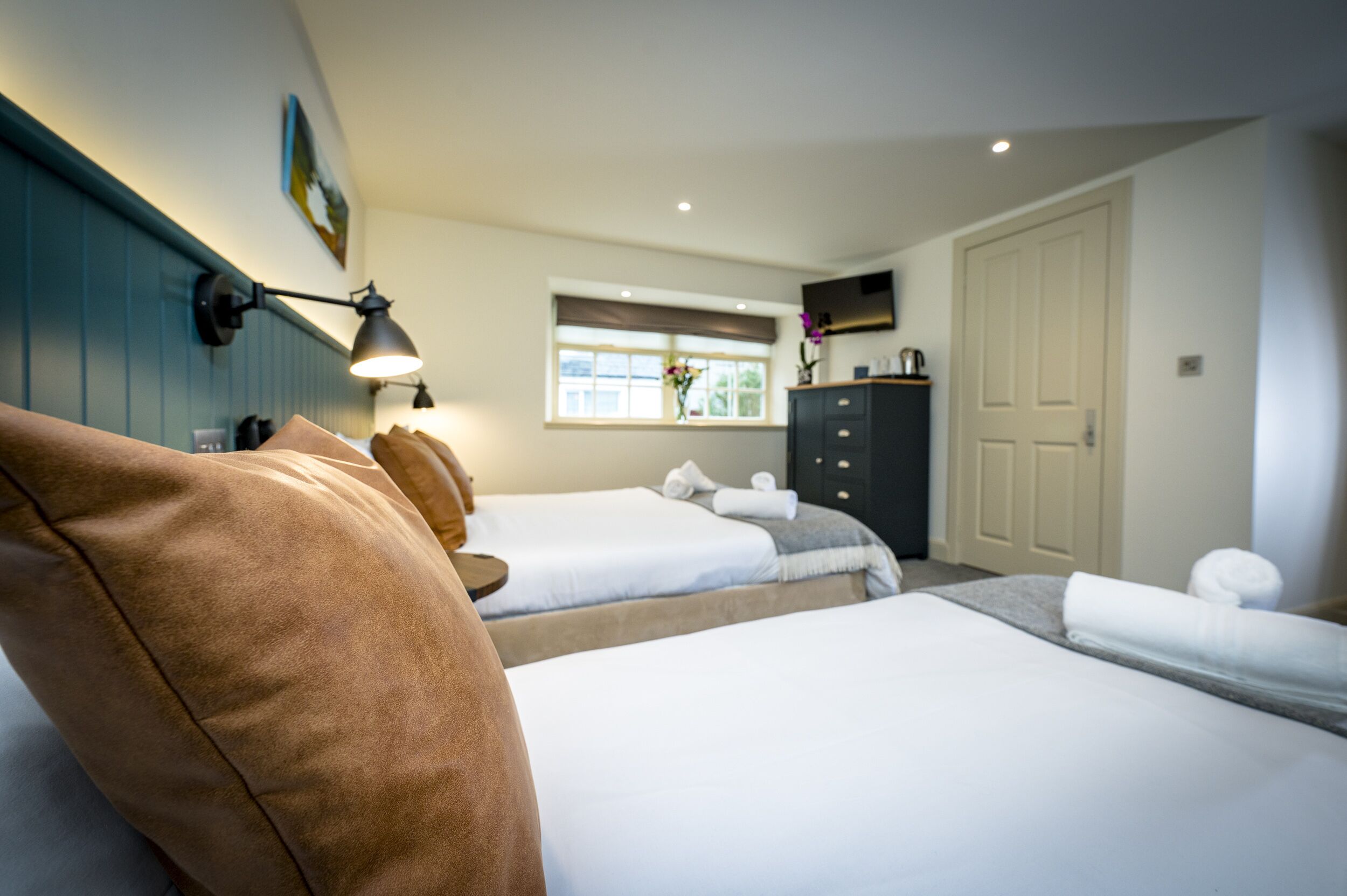 A hotel room with two beds, a dresser, a window with a view, and a flat-screen TV on the wall.