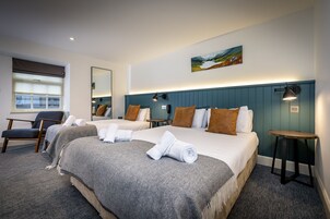 Habitación de hotel con dos camas, una silla, una mesita y un cuadro en la pared.
