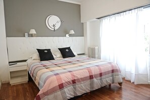 A bedroom with a large bed, two bedside tables, a wall clock, and a window with curtains. - Dodo Suites (Mar del Plata)