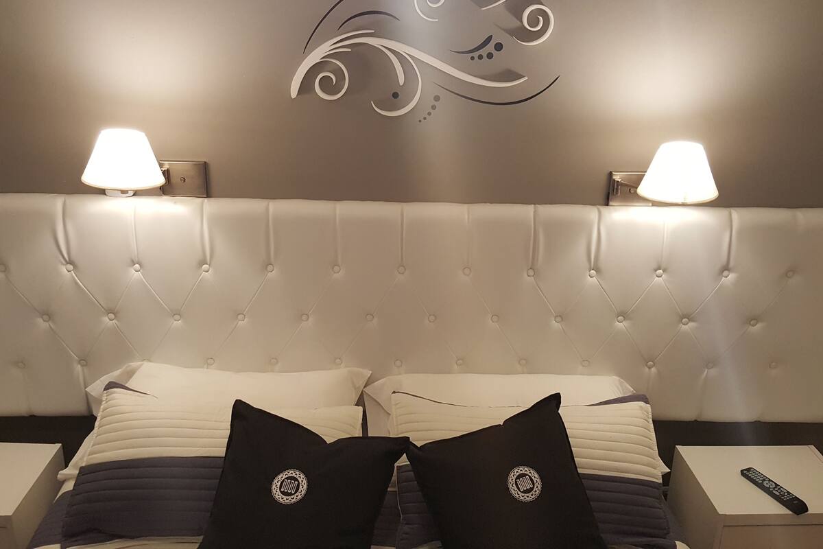A bedroom with a tufted headboard, two bedside lamps, a remote control, and decorative pillows.