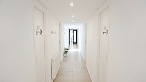 Een smalle, witte gang met deuren waarop 307 en 304 staat, die leidt naar een lichte kamer.