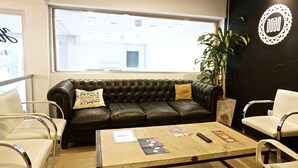 Een moderne zithoek met een leren bank, witte stoelen, een houten bijzettafeltje en een groot raam.