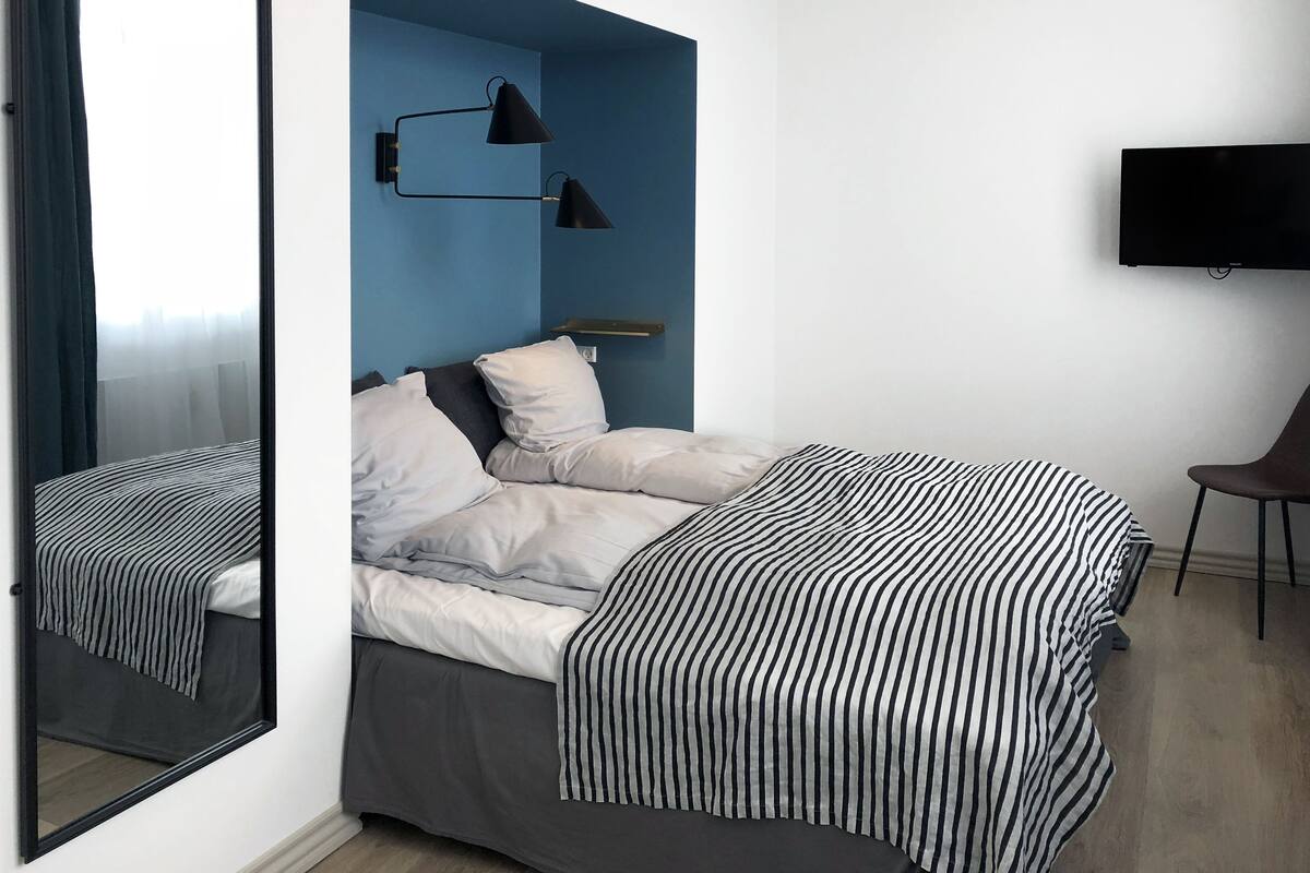 Une chambre moderne avec un lit, un grand miroir, une télévision et un mur d’accent bleu.