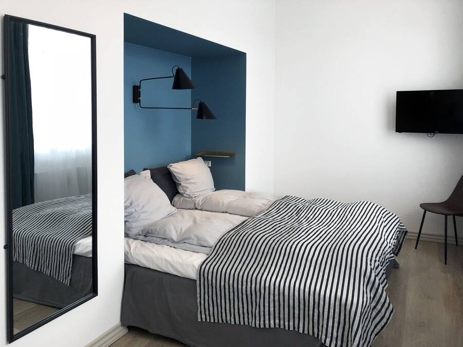 Un dormitorio moderno con cama, un espejo grande, televisión y una pared azul de acento.