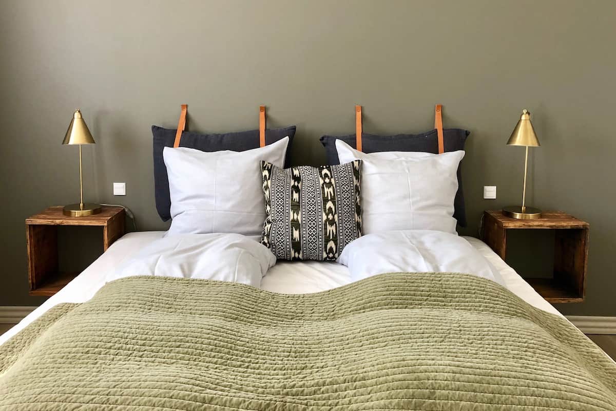 Un lit recouvert d’une couette verte, deux tables de chevet avec des lampes et une tête de lit ornée de trois oreillers.