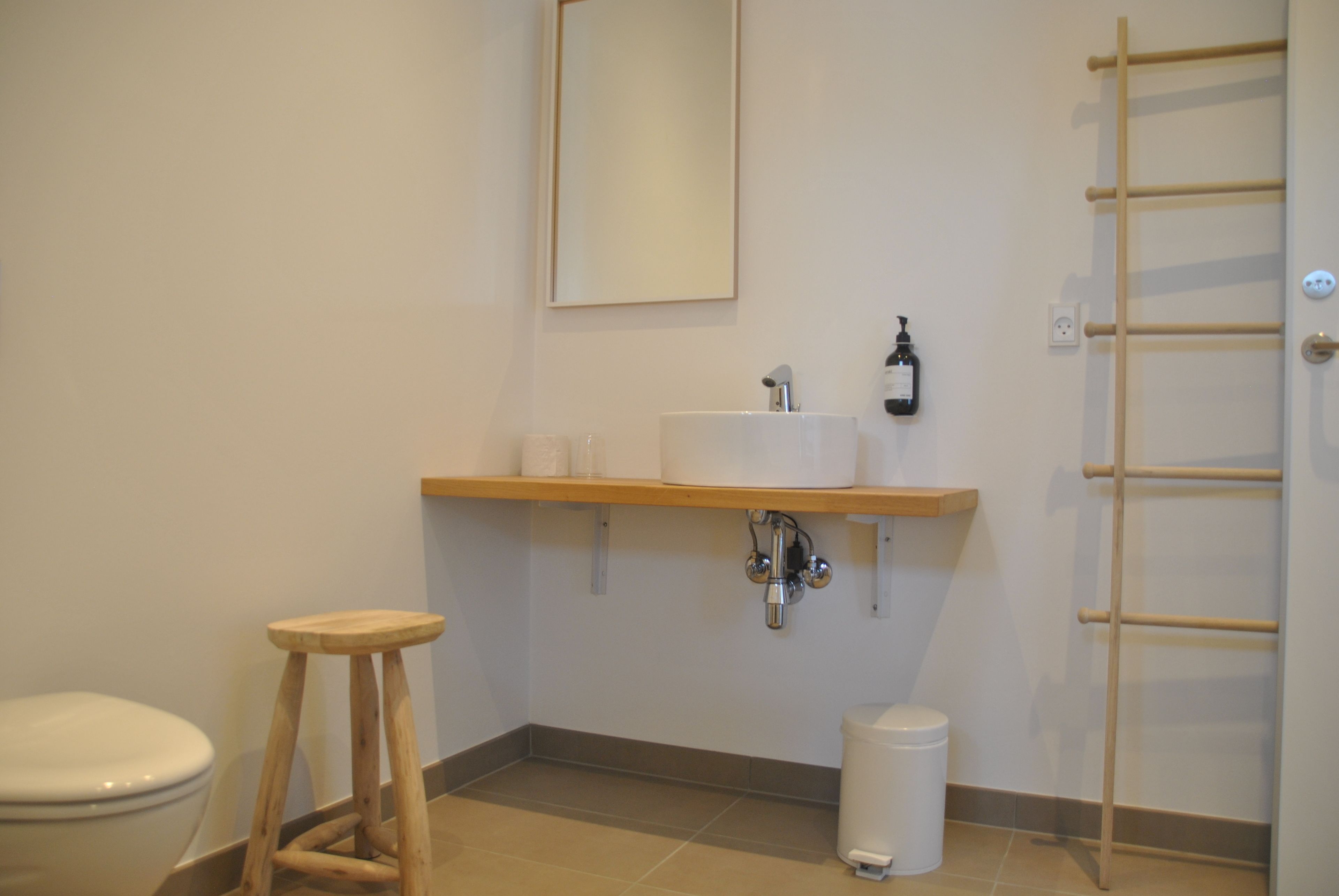 A bathroom with a toilet, wooden stool, sink, mirror, and towel rack.