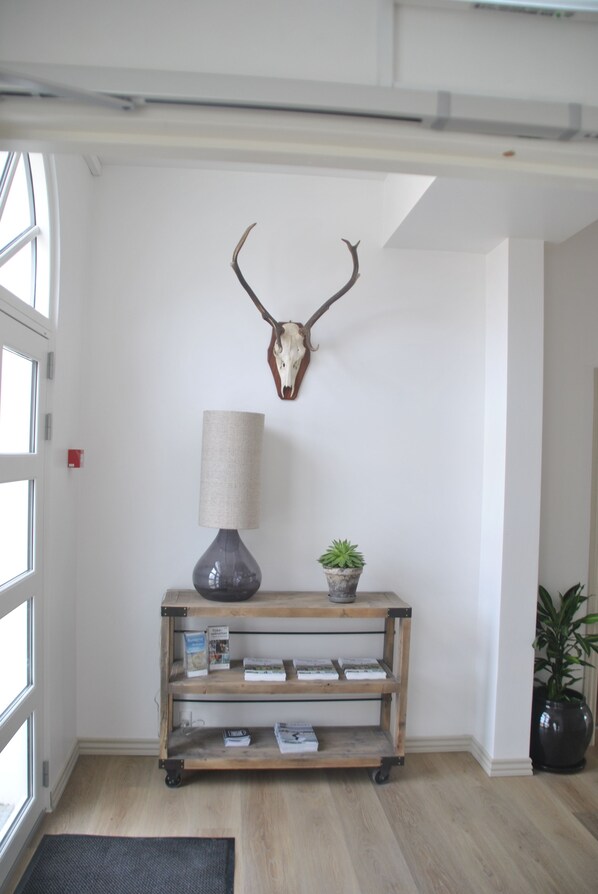 A room with a wooden console table, a lamp, a potted plant, and a mounted animal skull on the wall. - Hotel VANDret (Lokken)