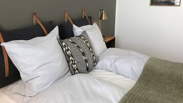 A neatly made bed with white and patterned pillows, a green throw blanket, and a wooden headboard.