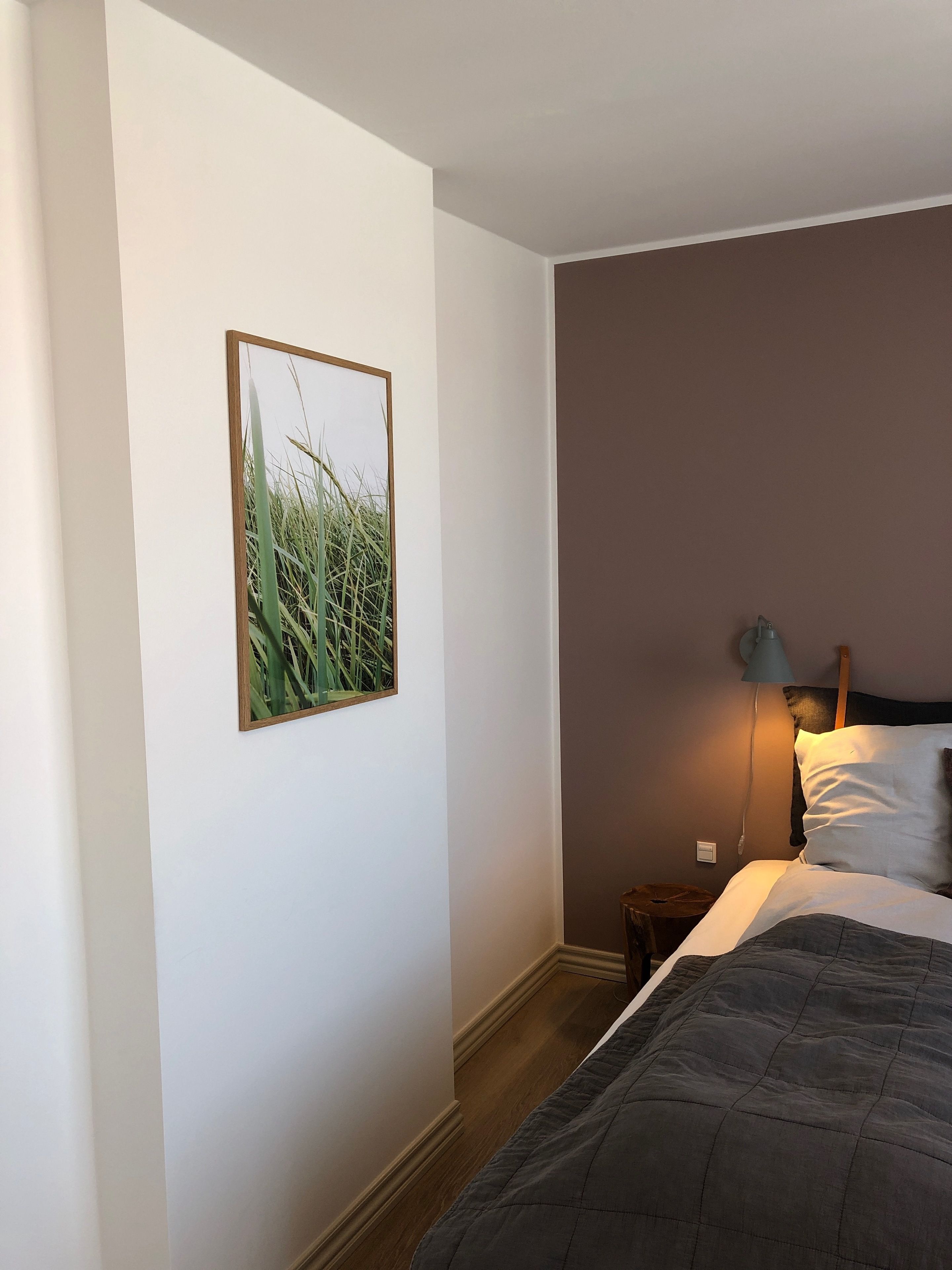 Et soveværelse med en seng, et natbord, en lampe og et billede i ramme på væggen.