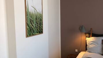 Un dormitorio con cama, mesita de noche, lámpara y un cuadro en la pared.