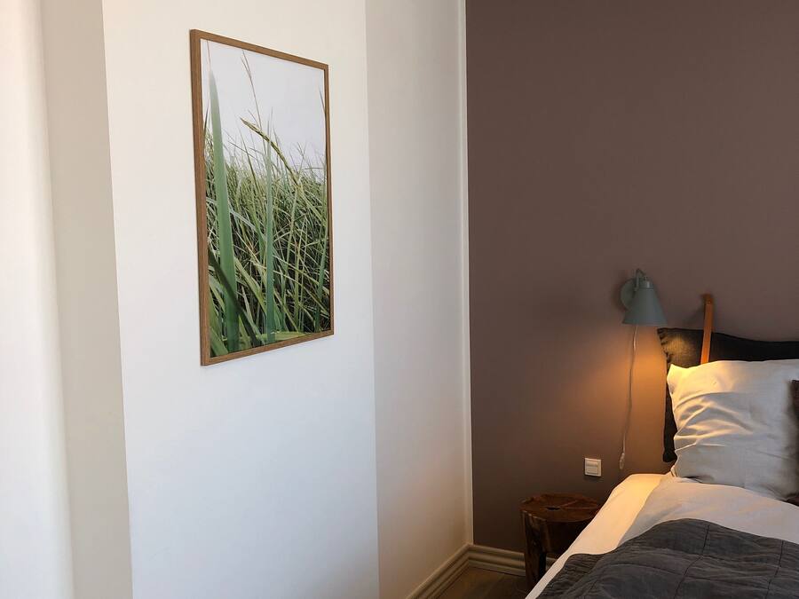 Un dormitorio con cama, mesita de noche, lámpara y un cuadro en la pared.