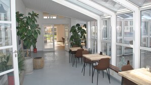 A modern interior with large windows, wooden tables, and chairs, and potted plants.